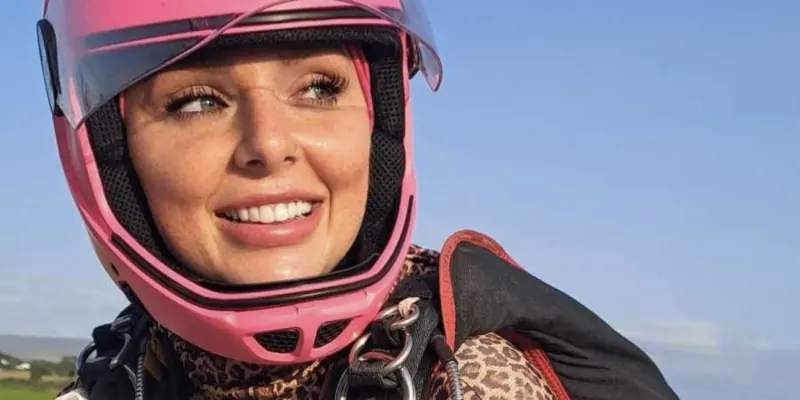 A jumper in a leopard-print suit and pink full-face helmet, geared up and smiling on the ground