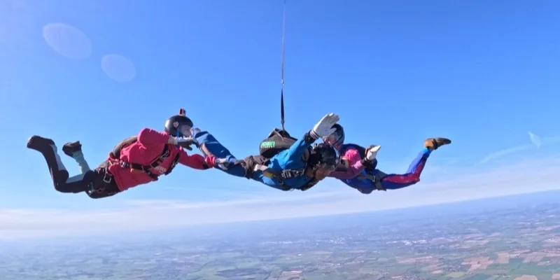 An instructor and a student in freefall alongside a tandem pair under drogue